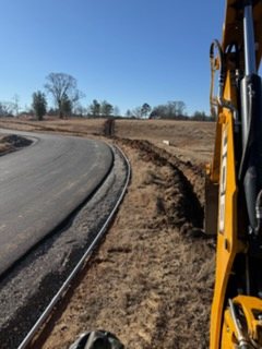 View from a backhoe cab of a trench dug beside a paved road.
