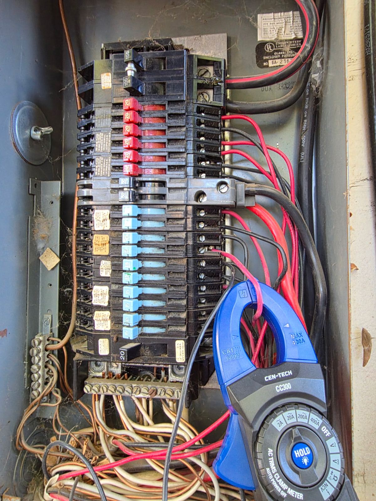 Open load center with a blue Cen-Tech CC300 clamp meter around a conductor.